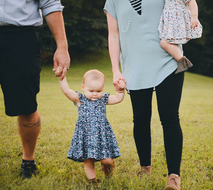 A toddler learning to walk with her parents